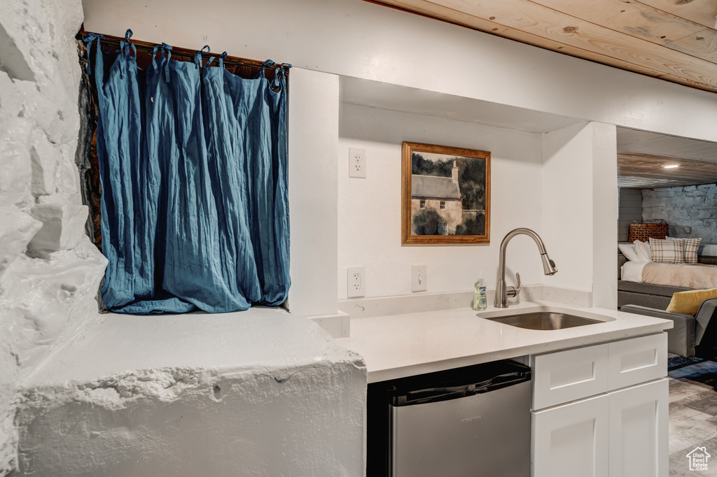 Kitchen featuring stainless steel dishwasher, white cabinetry, and light countertops