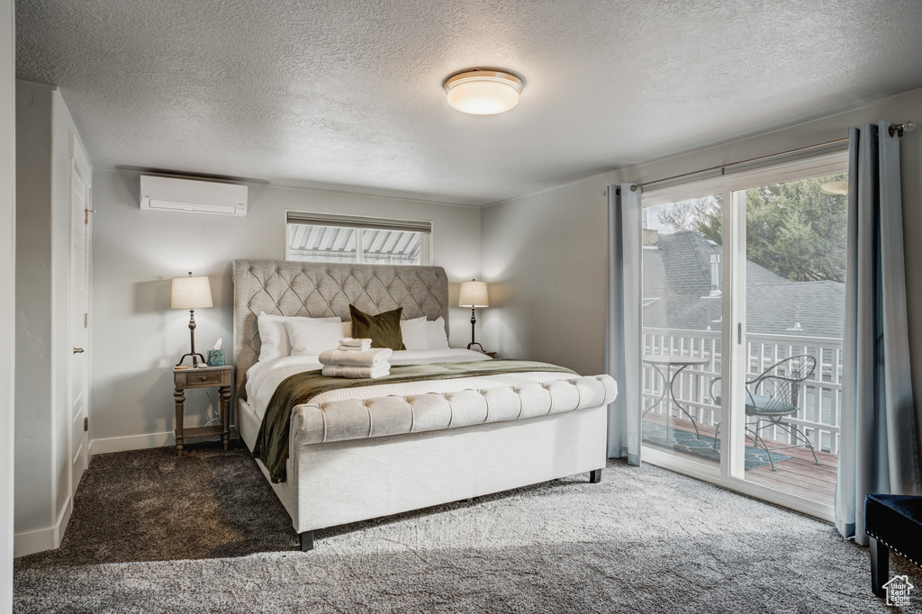 Carpeted bedroom featuring access to exterior, multiple windows, a textured ceiling, and a wall mounted air conditioner