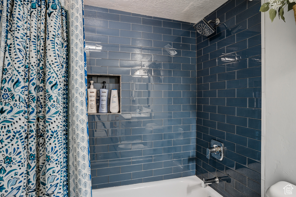 Bathroom featuring a textured ceiling and shower / bath combination with curtain