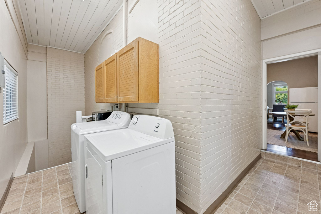 Laundry room with independent washer and dryer, cabinet space, brick wall, light tile patterned floors, and arched walkways