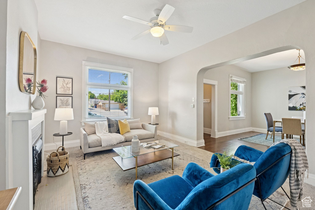 Living area with arched walkways, wood finished floors, ceiling fan, and a fireplace