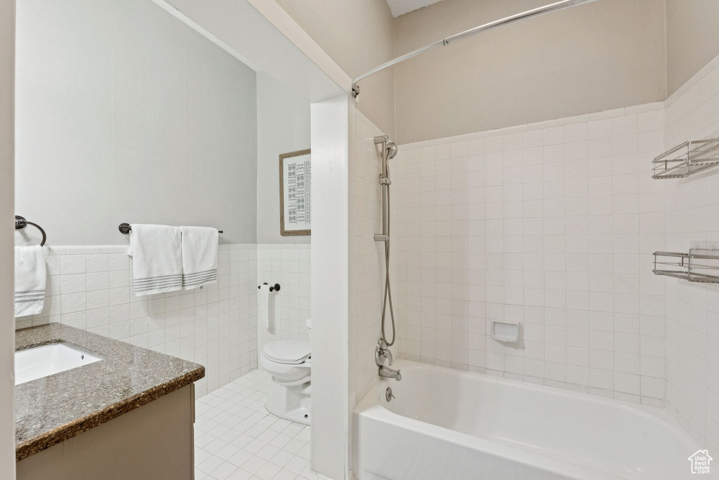 Bathroom featuring tile walls, washtub / shower combination, wainscoting, tile patterned floors, and vanity