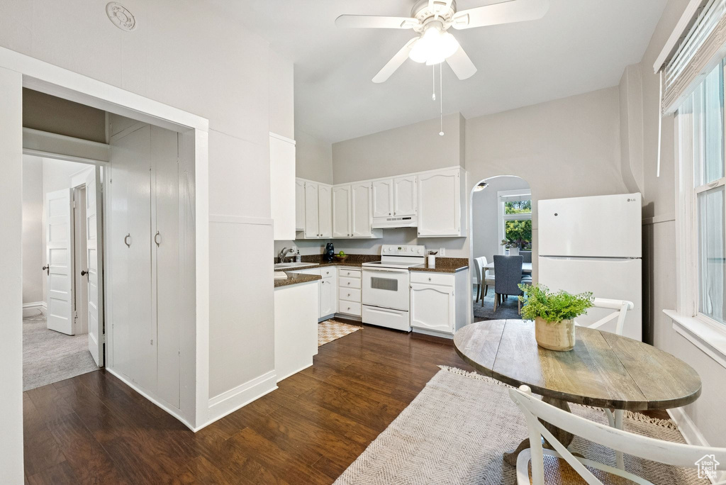 Kitchen with white appliances, arched walkways, under cabinet range hood, dark wood-type flooring, and white cabinetry