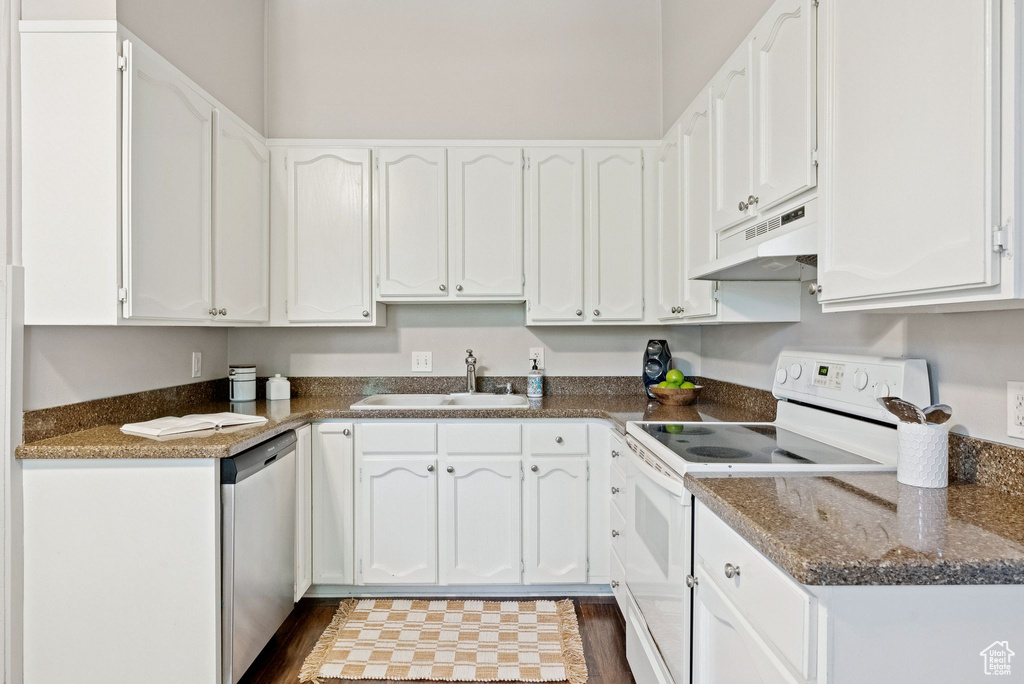 Kitchen with electric stove, stainless steel dishwasher, under cabinet range hood, white cabinetry, and dark countertops