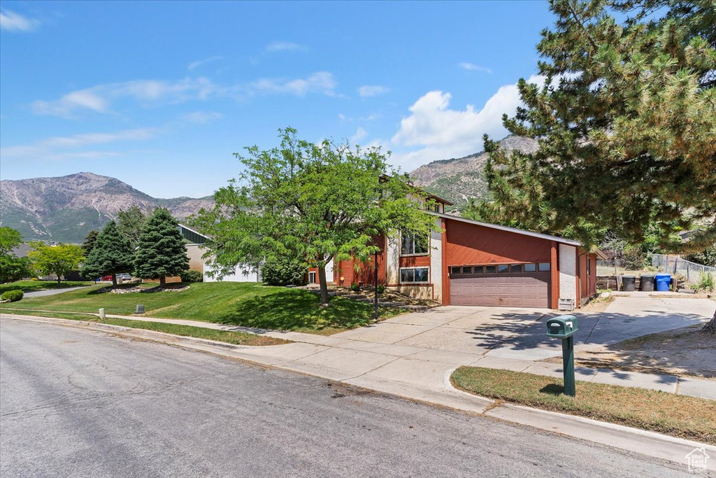 View of front of home featuring a mountain view, concrete driveway, a garage, and a front lawn