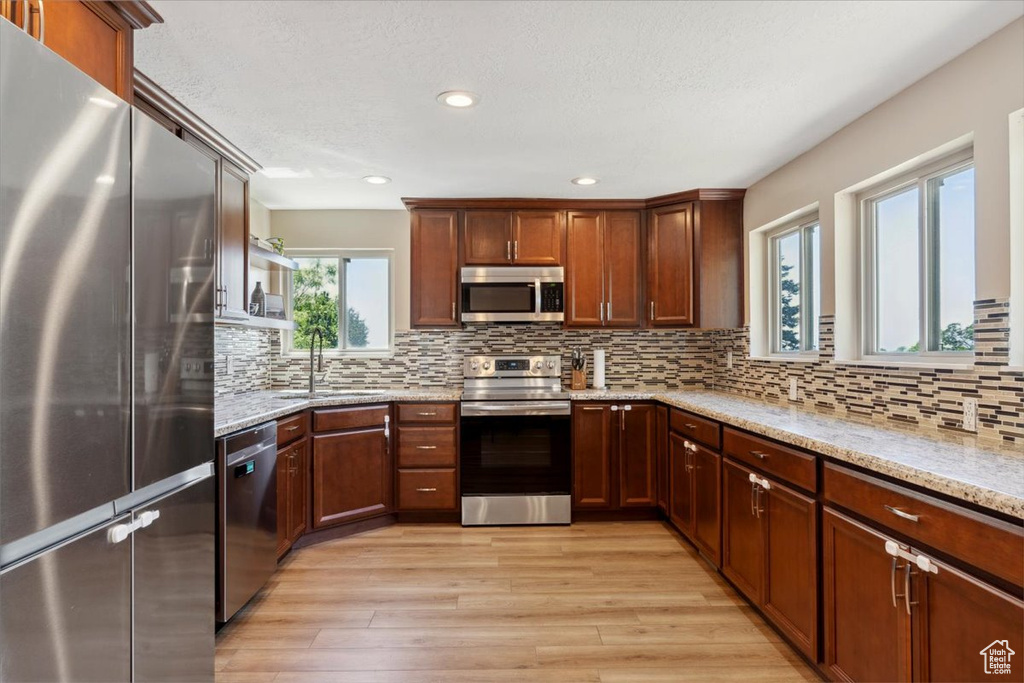 Kitchen featuring stainless steel appliances, light wood finished floors, light stone counters, recessed lighting, and backsplash