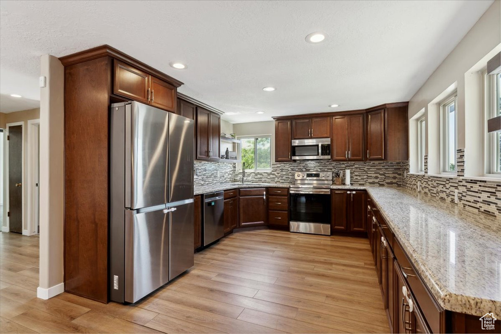 Kitchen with appliances with stainless steel finishes, light stone countertops, light wood finished floors, recessed lighting, and tasteful backsplash