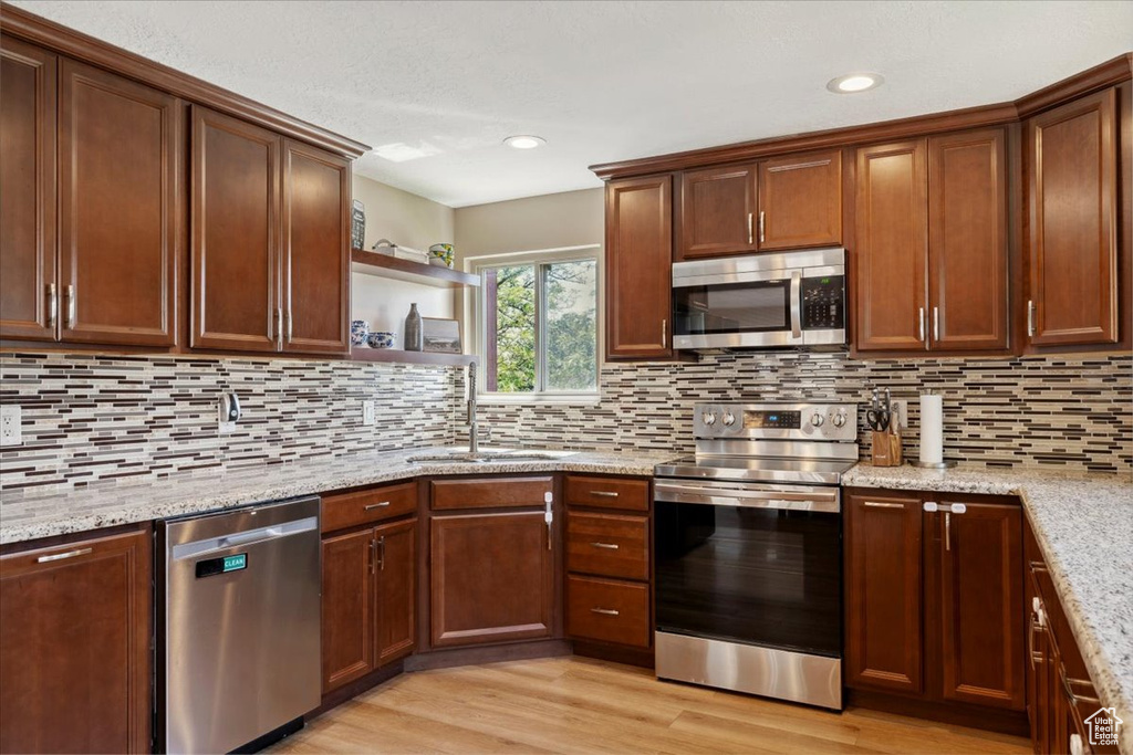 Kitchen featuring appliances with stainless steel finishes, open shelves, light stone counters, tasteful backsplash, and light wood finished floors