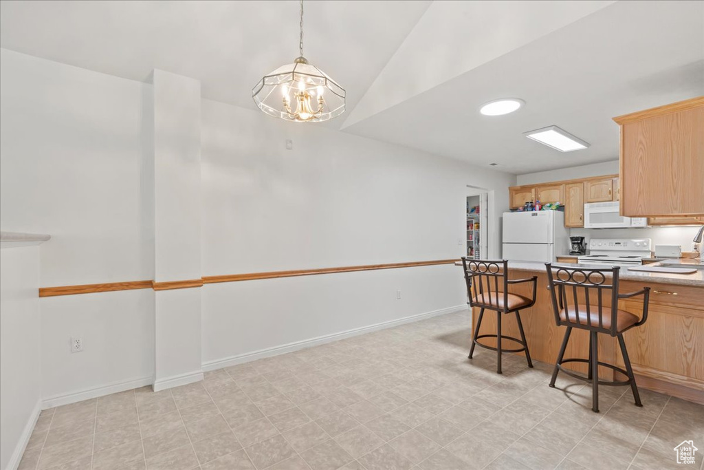Kitchen with white appliances, a chandelier, light countertops, light brown cabinets, and a kitchen breakfast bar
