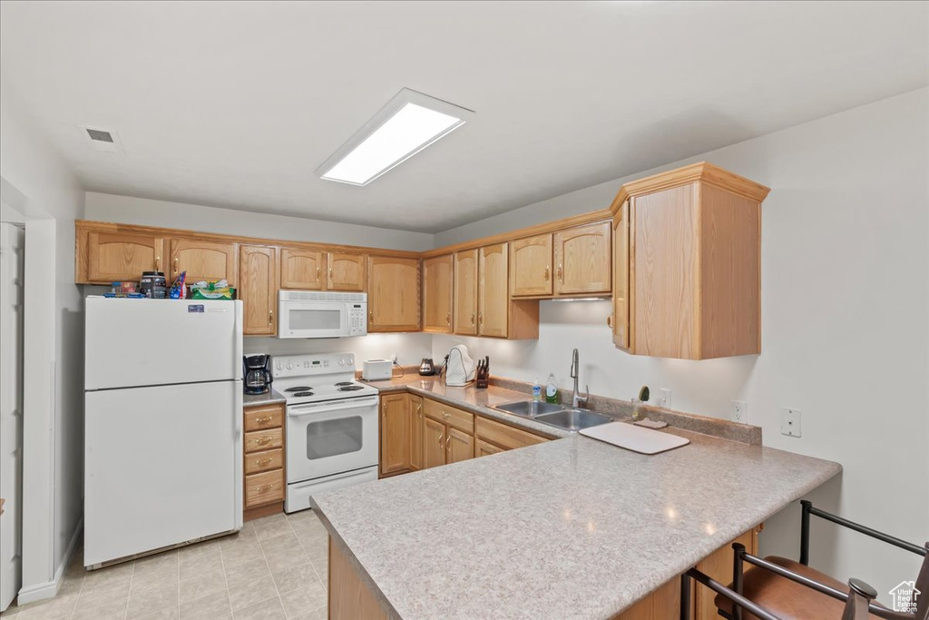 Kitchen with white appliances, a peninsula, light countertops, and light brown cabinets