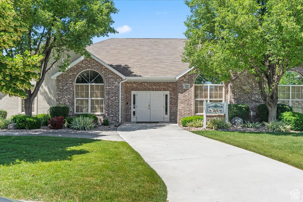 View of front of house with brick siding, a front yard, concrete driveway, and a shingled roof