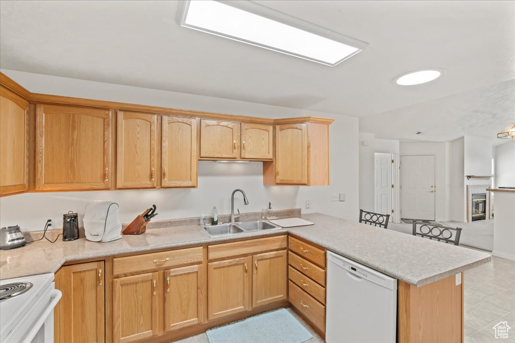 Kitchen with white dishwasher, a peninsula, light countertops, and stove