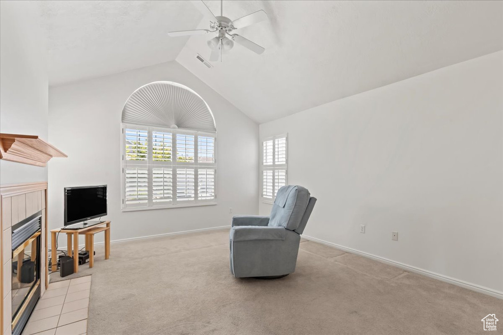 Living area featuring a tiled fireplace, a ceiling fan, light carpet, and vaulted ceiling