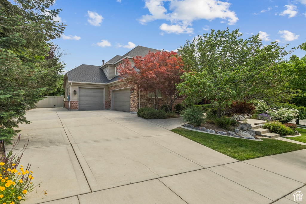 View of front of home with a garage, concrete driveway, brick siding, a gate, and a shingled roof