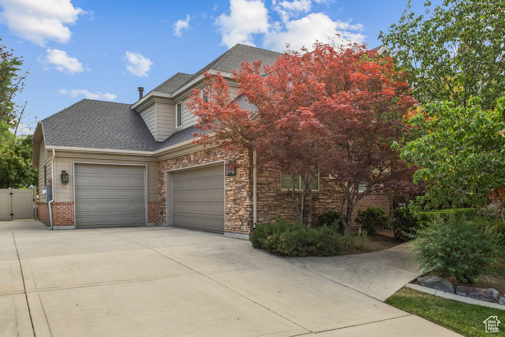 View of front of home with an attached garage, driveway, roof with shingles, a gate, and stone siding