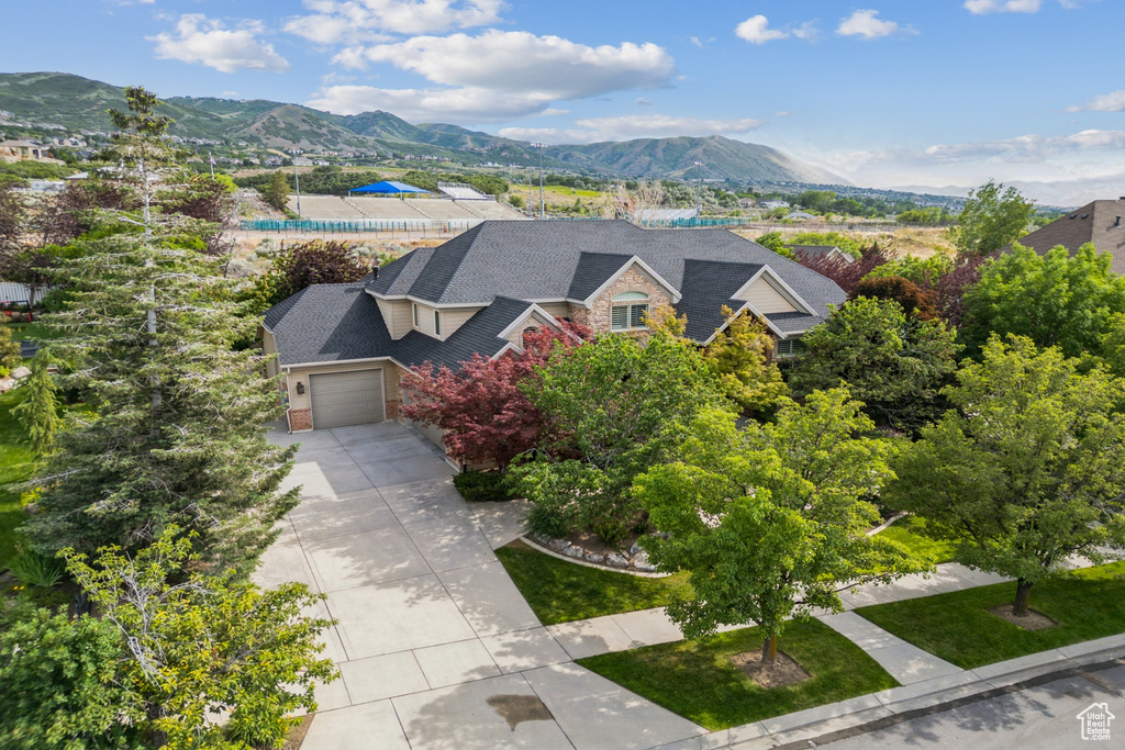 View of front of property featuring an attached garage, a mountain view, concrete driveway, and stone siding