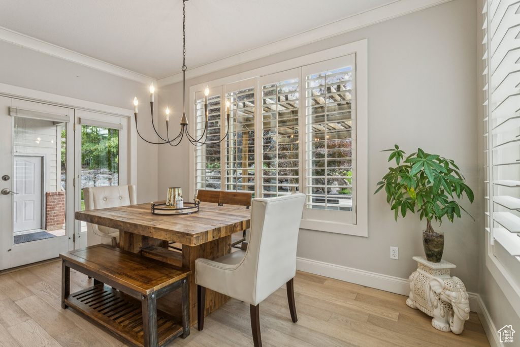 Dining area with light wood-style flooring, crown molding, and a chandelier