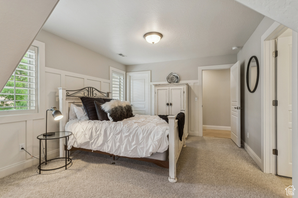 Bedroom featuring multiple windows, light colored carpet, and a decorative wall