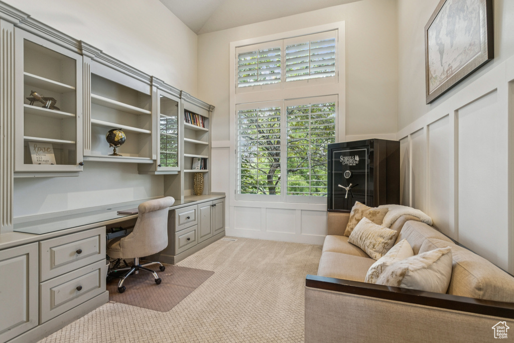 Office space with built in desk, a decorative wall, light carpet, lofted ceiling, and wainscoting