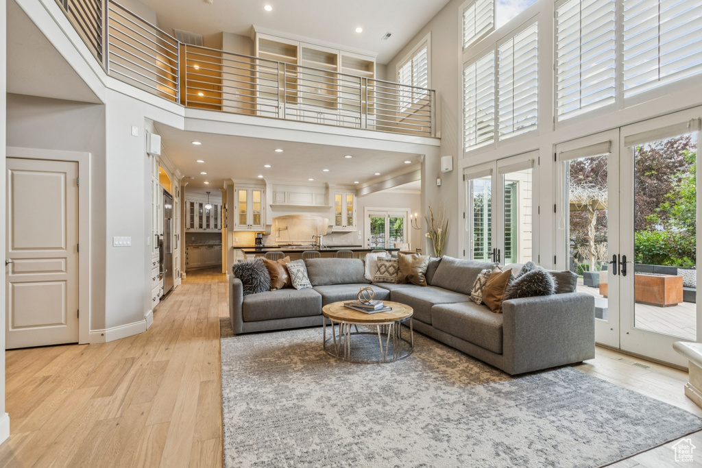 Living area with a towering ceiling, french doors, healthy amount of natural light, light wood-style floors, and recessed lighting