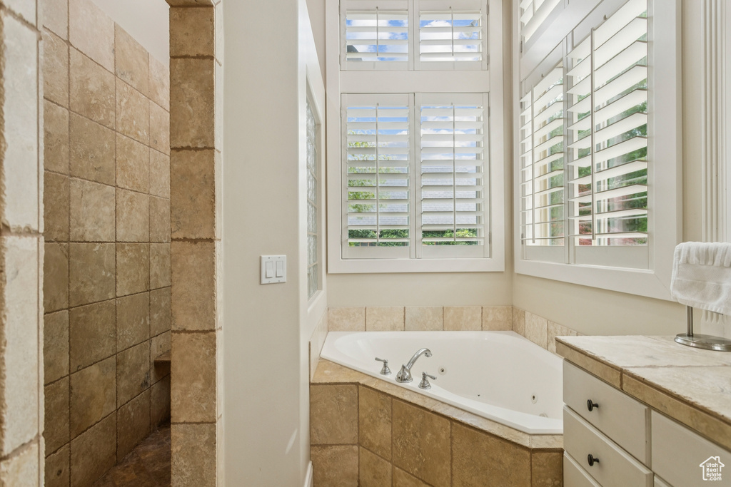 Full bathroom featuring plenty of natural light, a jetted tub, vanity, and tiled shower