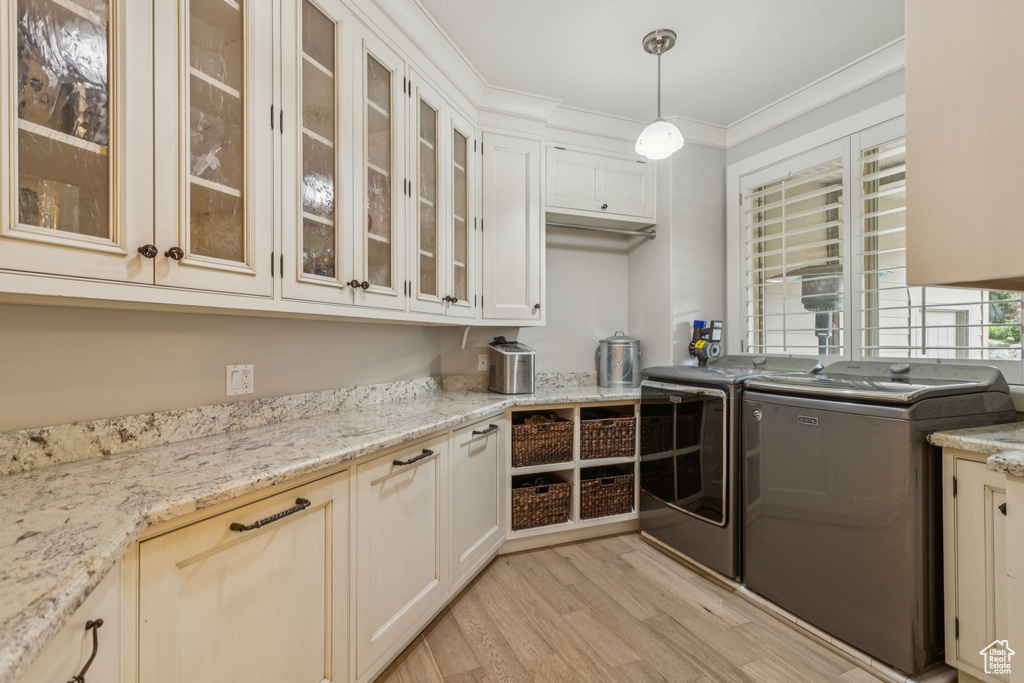 Kitchen featuring independent washer and dryer, light wood-style floors, crown molding, hanging light fixtures, and glass insert cabinets
