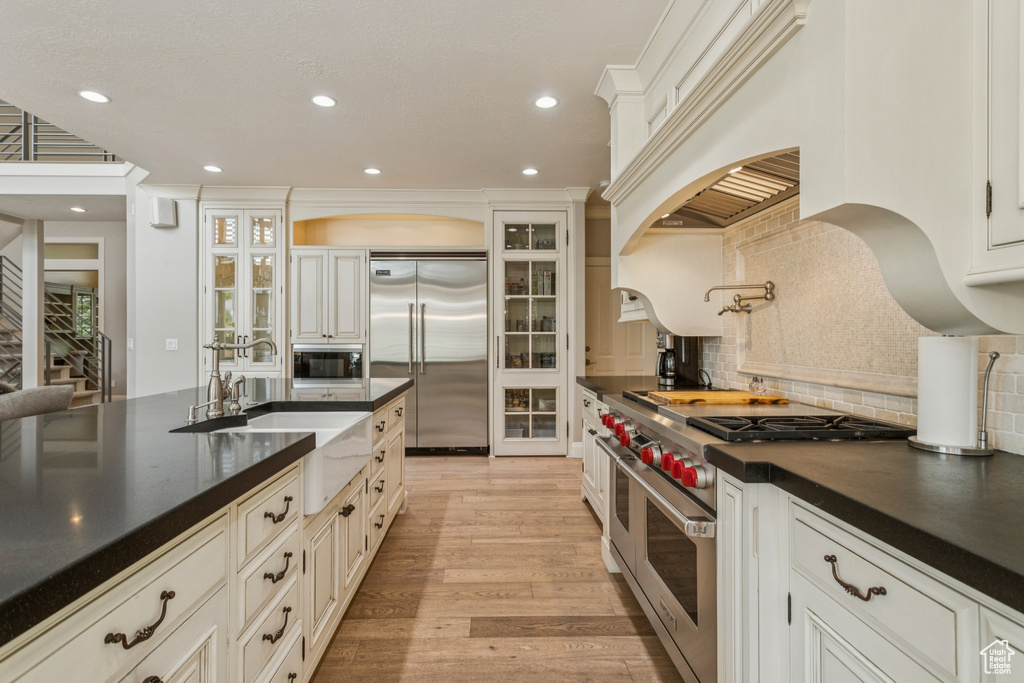 Kitchen featuring built in appliances, dark countertops, backsplash, recessed lighting, and light wood-type flooring