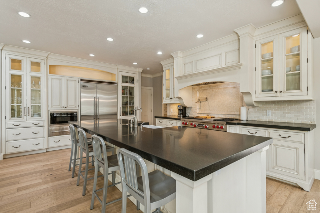 Kitchen with dark countertops, built in appliances, light wood-style flooring, decorative backsplash, and ornamental molding
