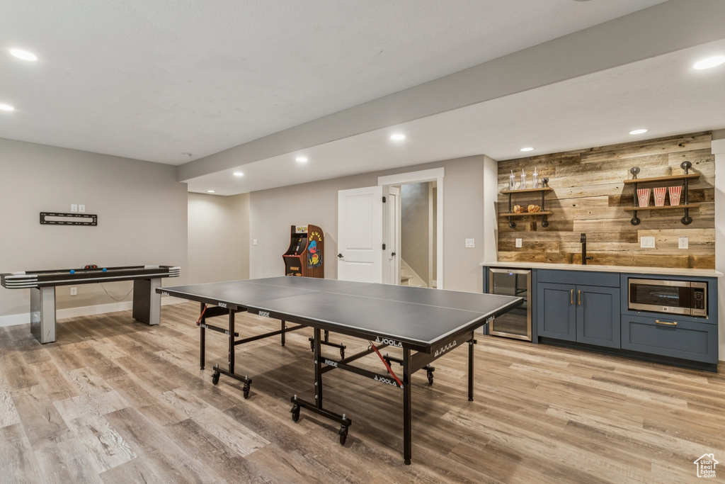Rec room featuring wine cooler, bar with sink, light wood finished floors, recessed lighting, and wood walls