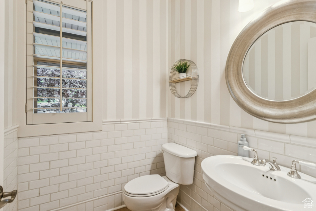 Half bath featuring wallpapered walls and wainscoting