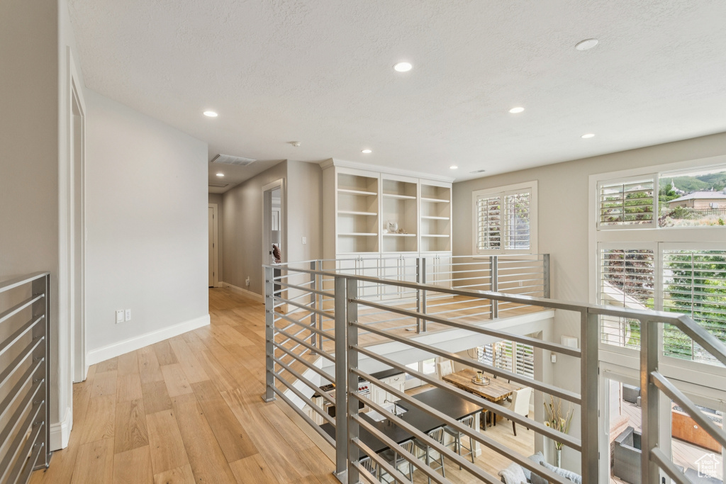 Hallway with light wood-style floors, recessed lighting, and an upstairs landing