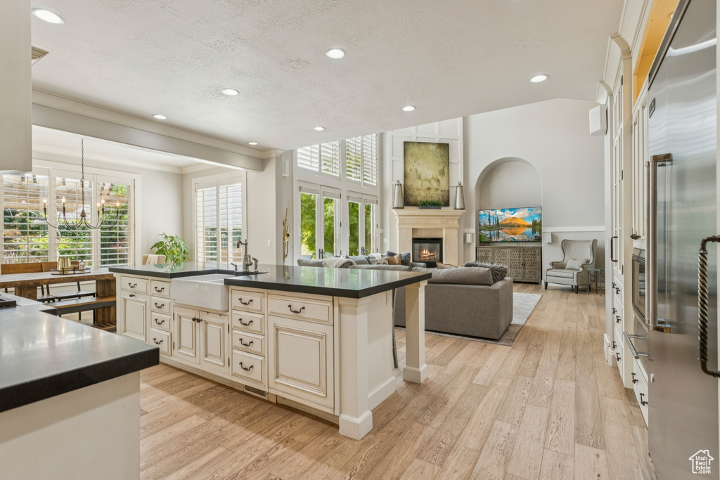 Kitchen featuring cream cabinets, dark countertops, a glass covered fireplace, light wood finished floors, and a chandelier
