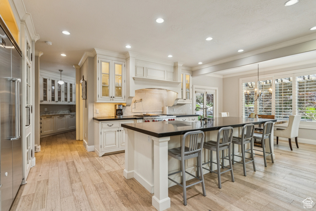 Kitchen with dark countertops, light wood finished floors, ornamental molding, tasteful backsplash, and recessed lighting