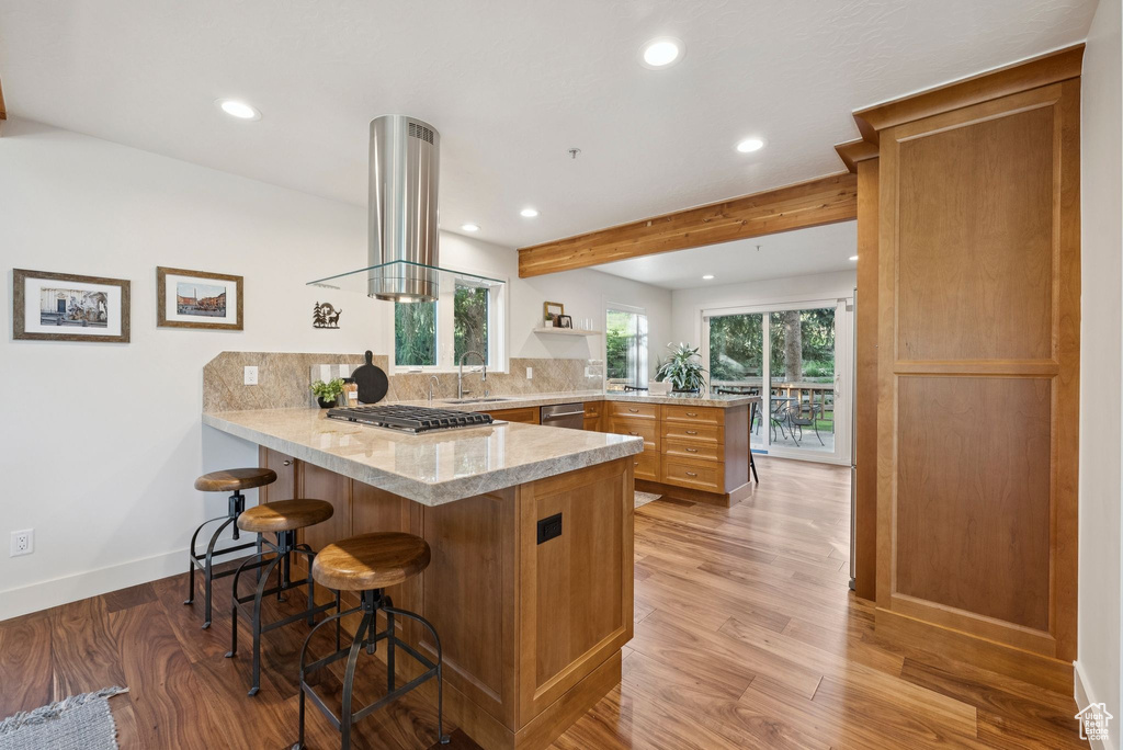 Kitchen with a peninsula, recessed lighting, light wood-style floors, light stone counters, and backsplash