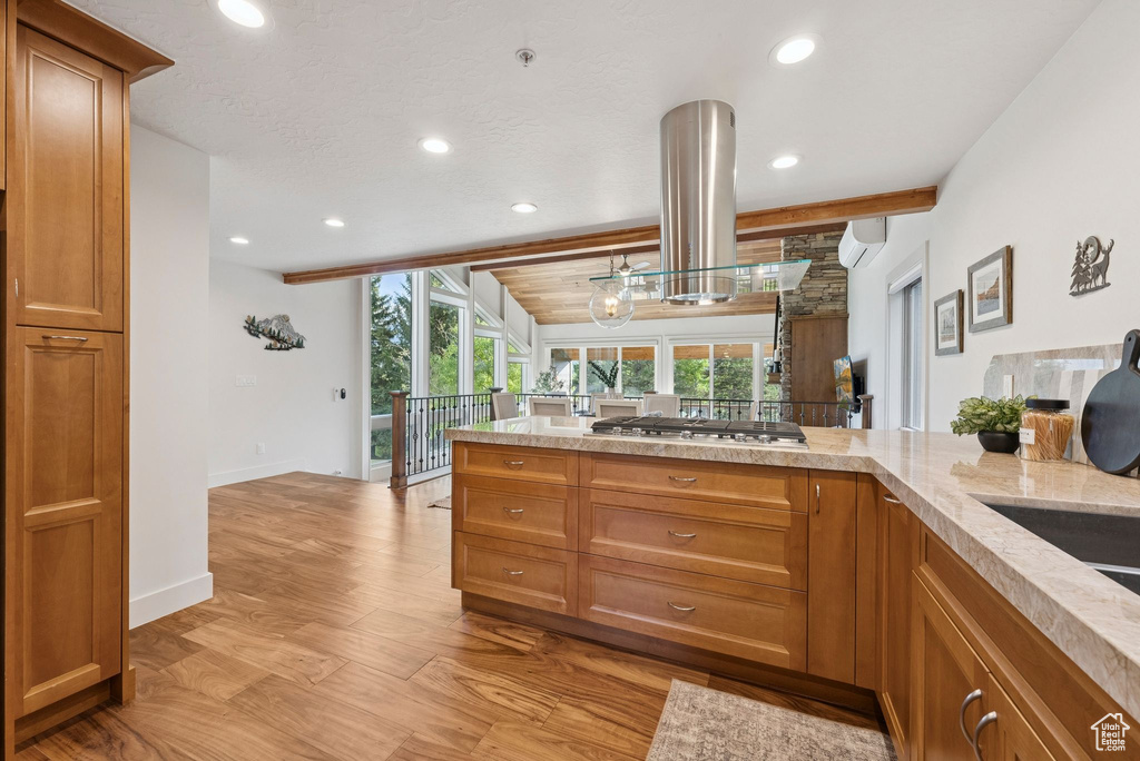 Kitchen featuring stainless steel gas cooktop, island range hood, light wood-type flooring, recessed lighting, and brown cabinets