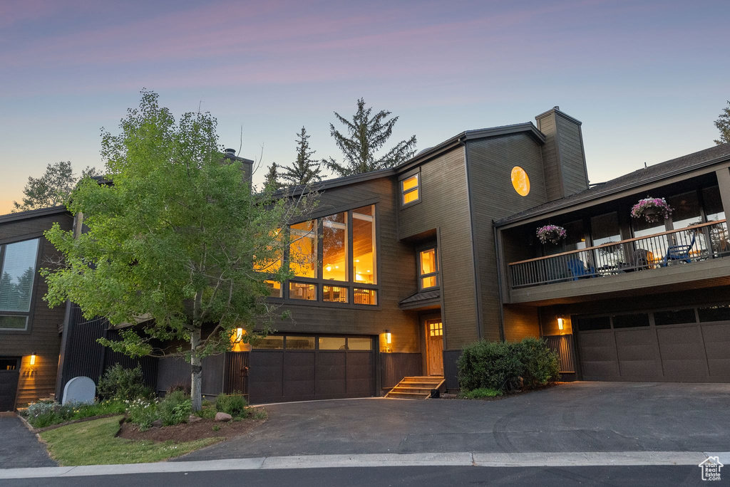 Contemporary home featuring a balcony, an attached garage, a chimney, and asphalt driveway