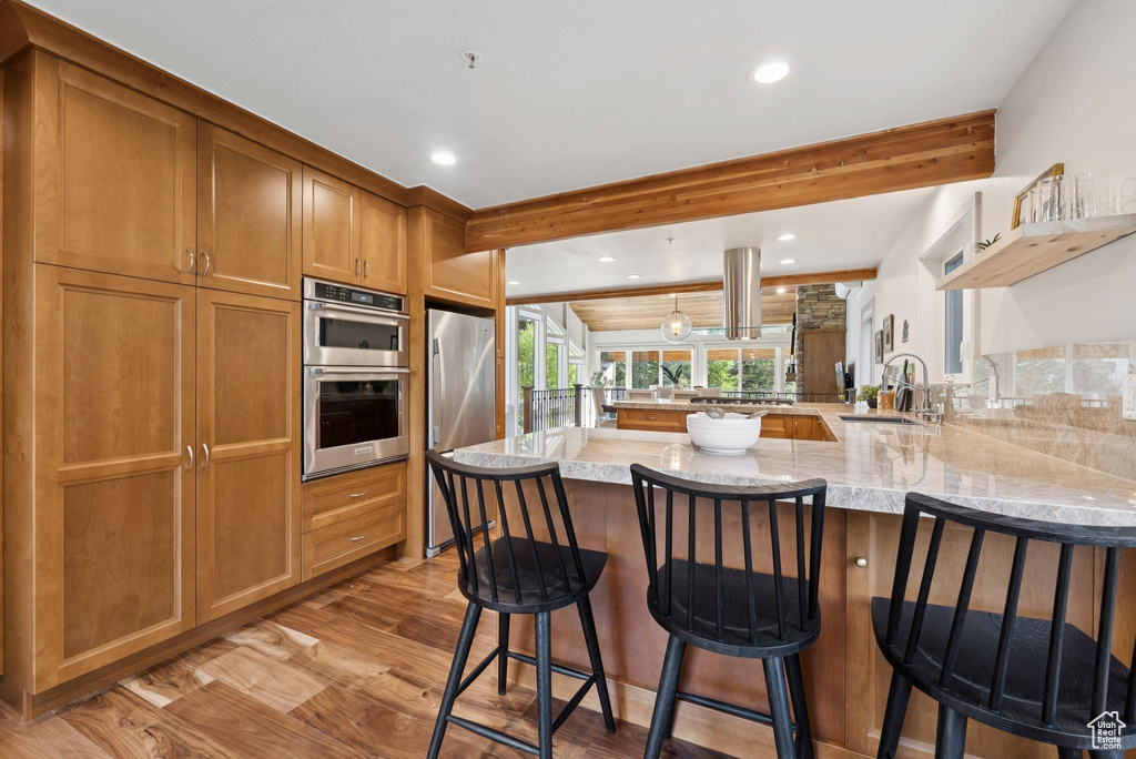 Kitchen with a peninsula, stainless steel appliances, light stone countertops, beam ceiling, and recessed lighting