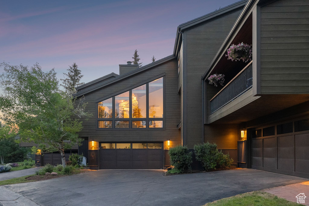 View of front of property featuring asphalt driveway, a chimney, and an attached garage