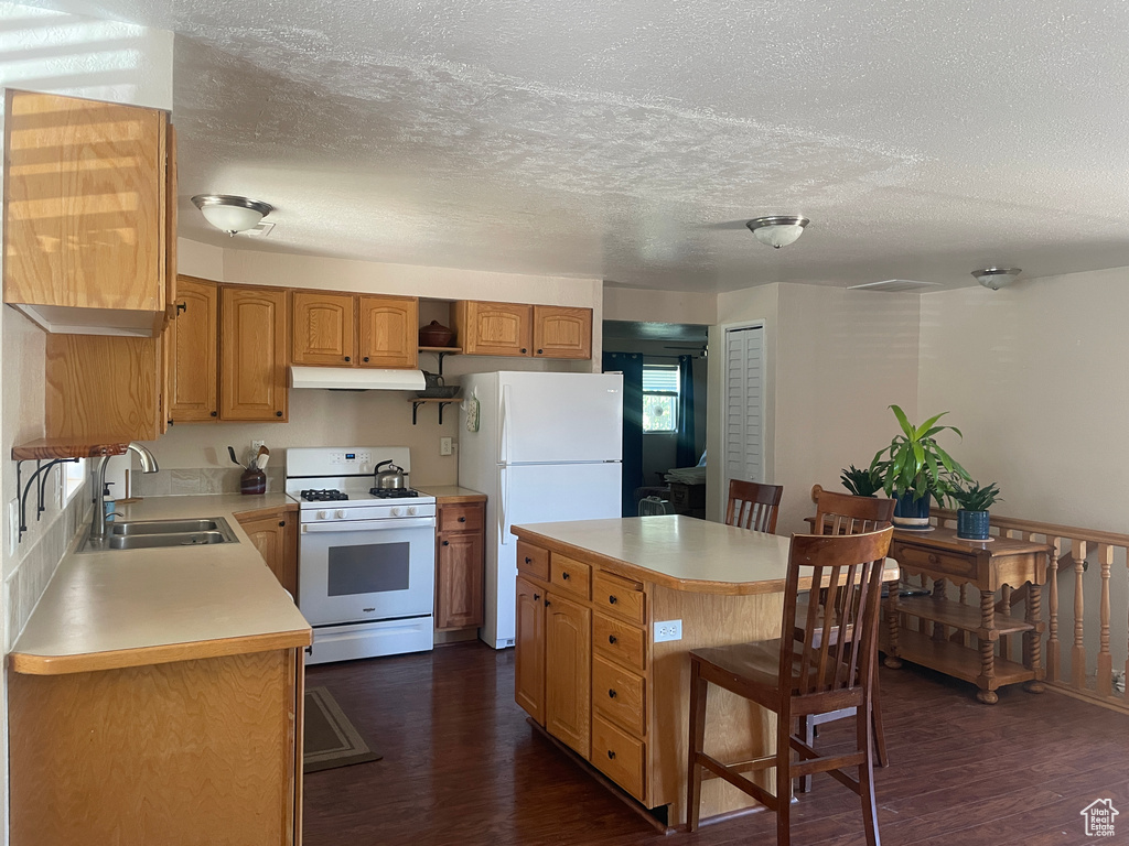 Kitchen with white appliances, dark wood-style floors, light countertops, a kitchen island, and a breakfast bar area