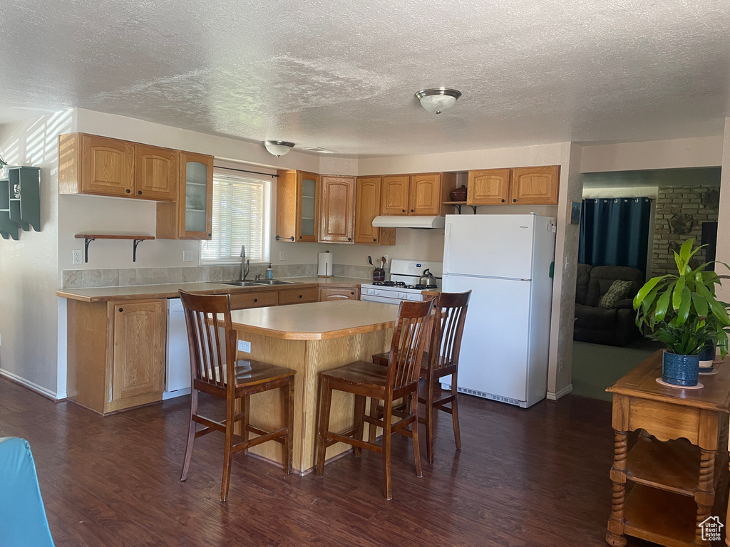 Kitchen featuring white appliances, under cabinet range hood, light countertops, glass insert cabinets, and a textured ceiling