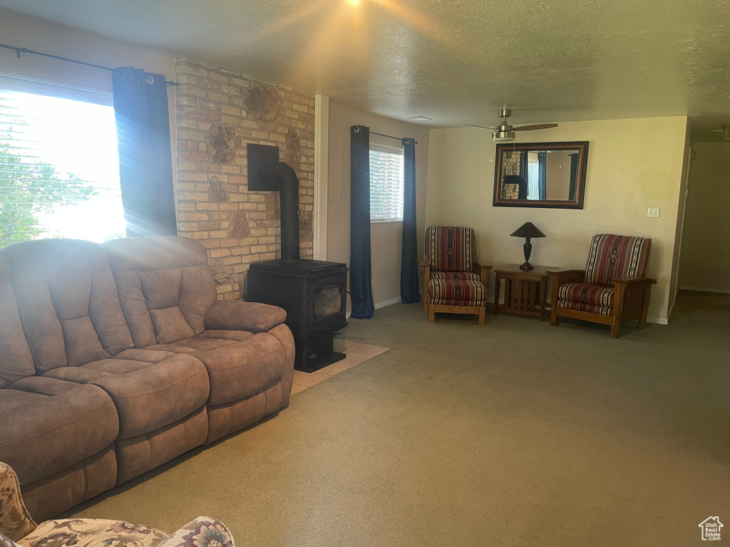 Carpeted living area featuring a textured ceiling, a ceiling fan, and a wood stove