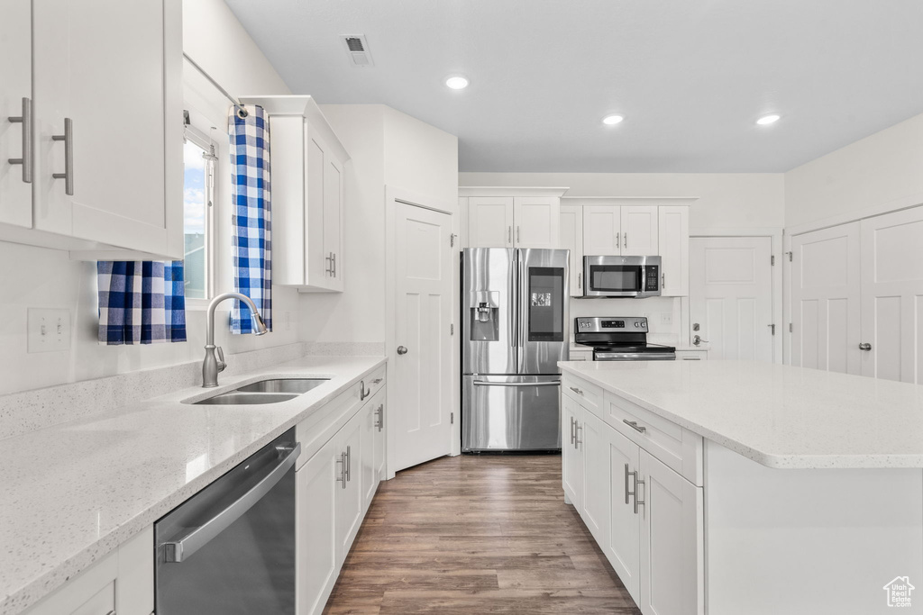 Kitchen featuring stainless steel appliances, white cabinetry, wood finished floors, recessed lighting, and light stone countertops