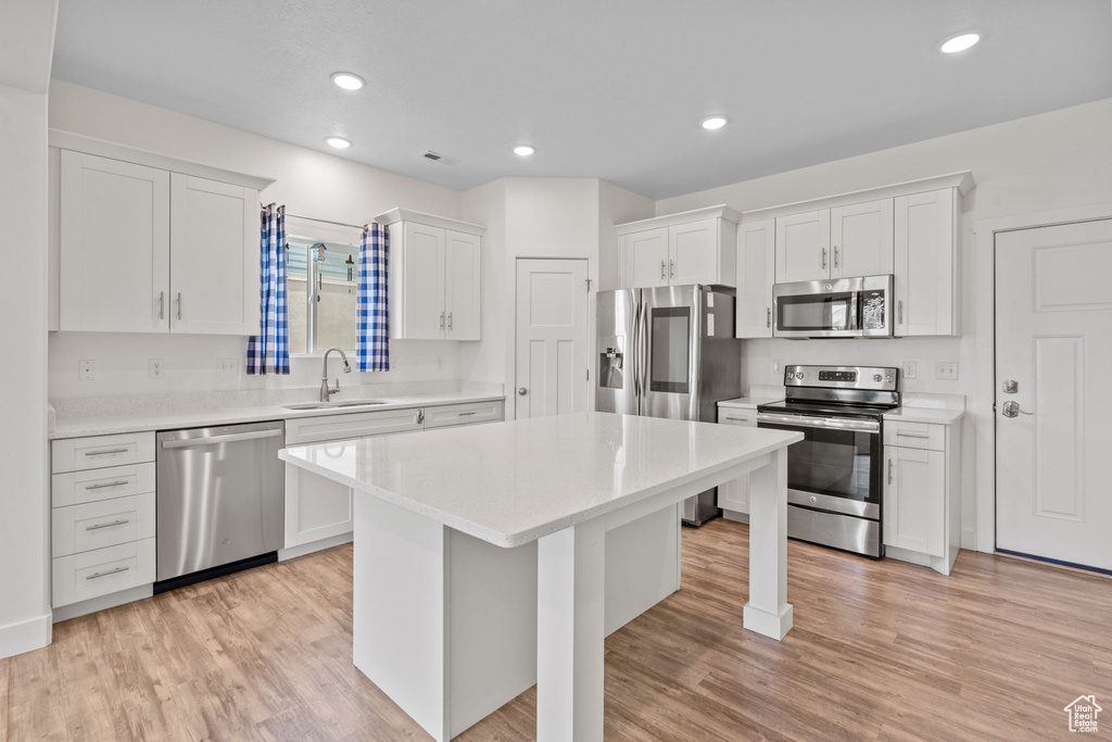 Kitchen featuring stainless steel appliances, white cabinets, a center island, light countertops, and light wood-type flooring
