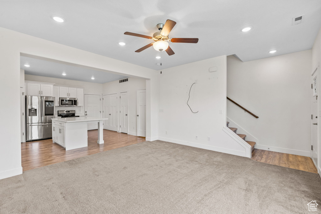 Unfurnished living room featuring light carpet, a ceiling fan, stairway, recessed lighting, and light wood-style flooring