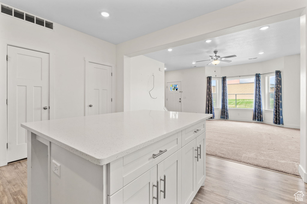 Kitchen with recessed lighting, a kitchen island, light wood-type flooring, white cabinets, and light stone countertops