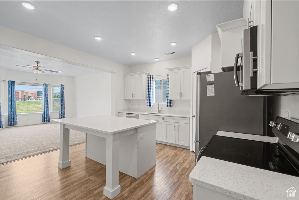 Kitchen featuring range with electric stovetop, light wood-style flooring, white cabinetry, a center island, and recessed lighting