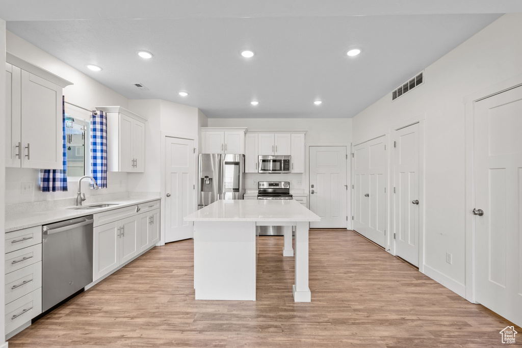 Kitchen featuring appliances with stainless steel finishes, white cabinetry, a center island, light countertops, and light wood-type flooring