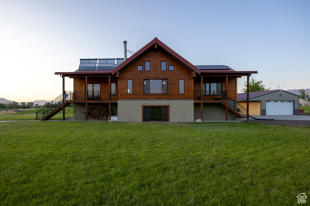 Back of property at dusk with stairs, roof mounted solar panels, a yard, and a detached garage