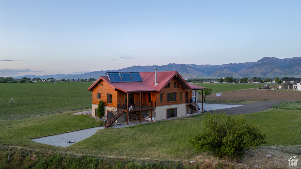 View of front of home with stairway, roof mounted solar panels, a front lawn, and a mountain view