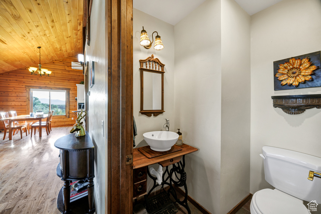 Half bath featuring wood walls, a chandelier, wood finished floors, vaulted ceiling, and wood ceiling